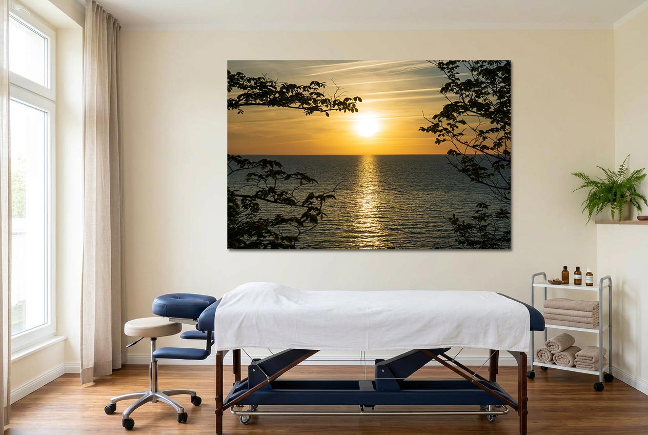 Behandlungsraum Naturheilkunde: XXL Meerbild mit Sonnenuntergang durch Bäume zentral über der Behandlungsliege neben Rollwagen mit Ölen.