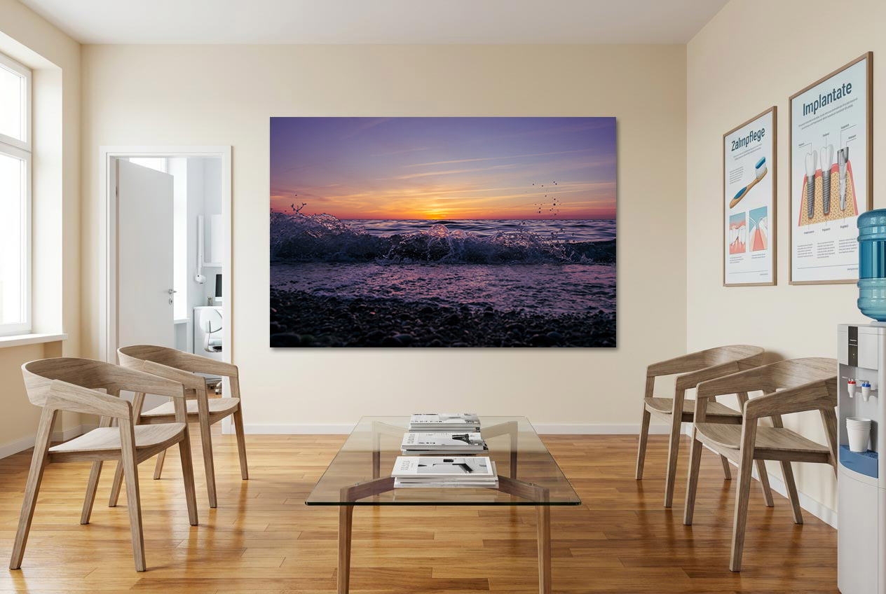 Bilder für Praxis: XXL Wandbild mit Sonnenuntergang in Lila-Violett und sanfter Gischtwelle im Wartezimmer über einem Glastisch.